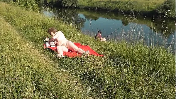 Vroča MILF sexy Frina on river bank undressed and sunbathes naked. Random man fisherman watching for her, and in the end decided to join naked woman. Wild beach. Nudist beach. Public nudity. Public exposure. Naked in public sveža cev